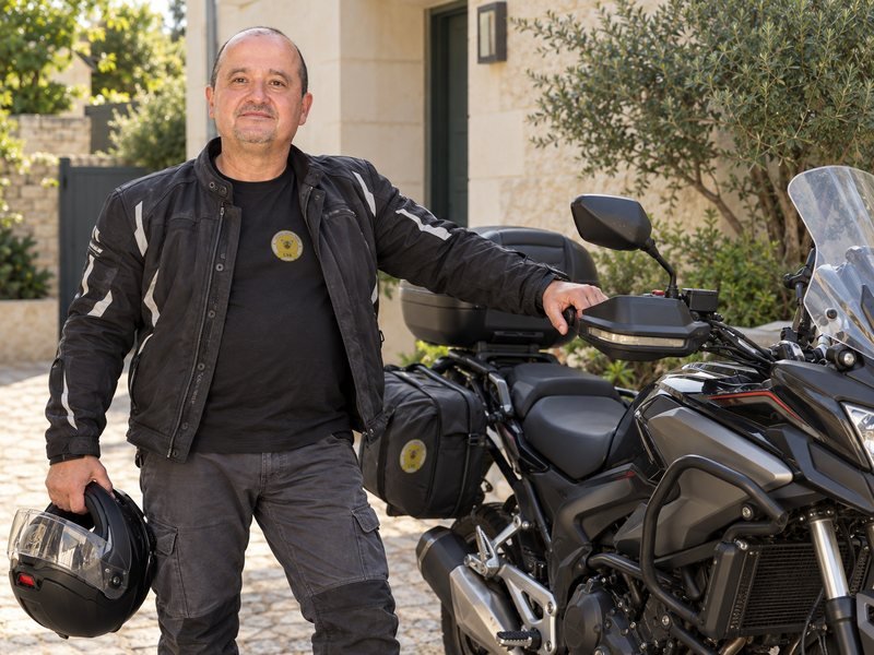Image générée par IA d’après des photos d’Éric : Éric Bessa près de sa moto, casque à la main